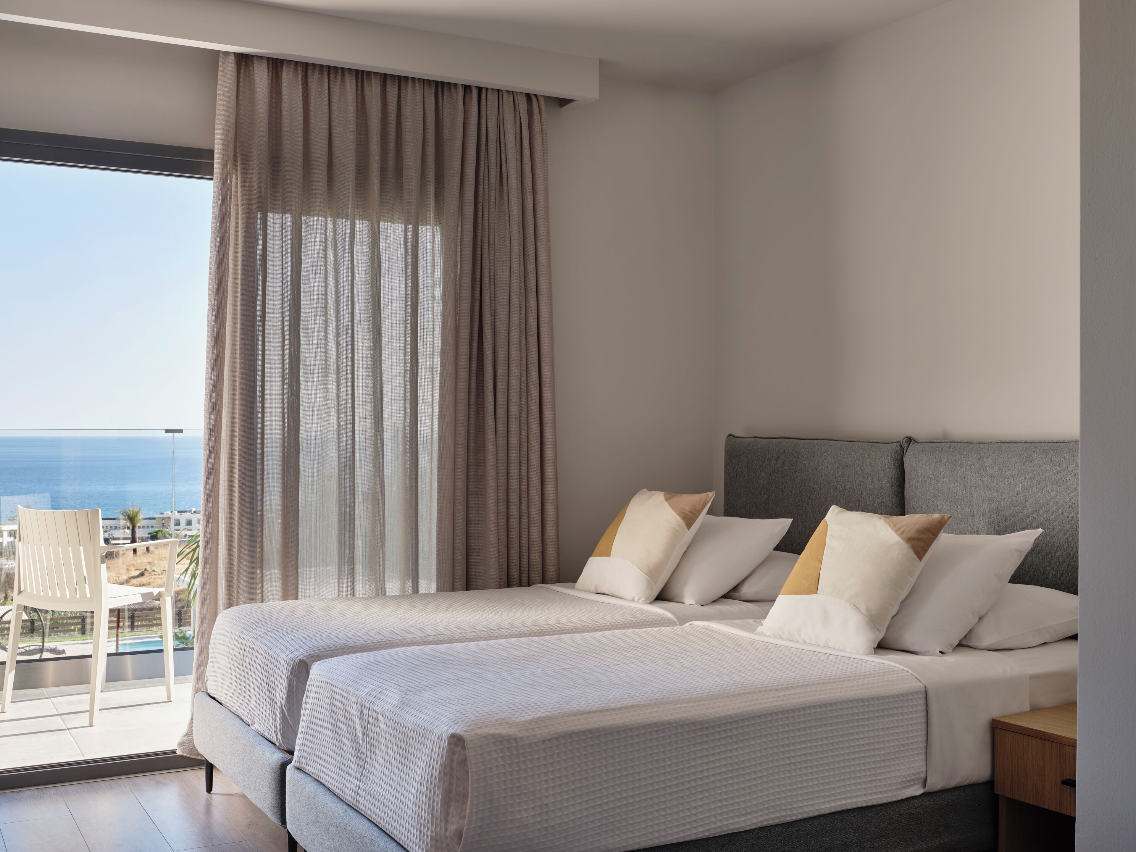 A hotel room with two beds, a balcony, and a view of the sea.