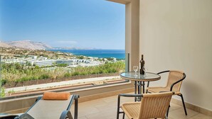 A balcony with a table and chairs, a wine glass, and a view of the sea and buildings.