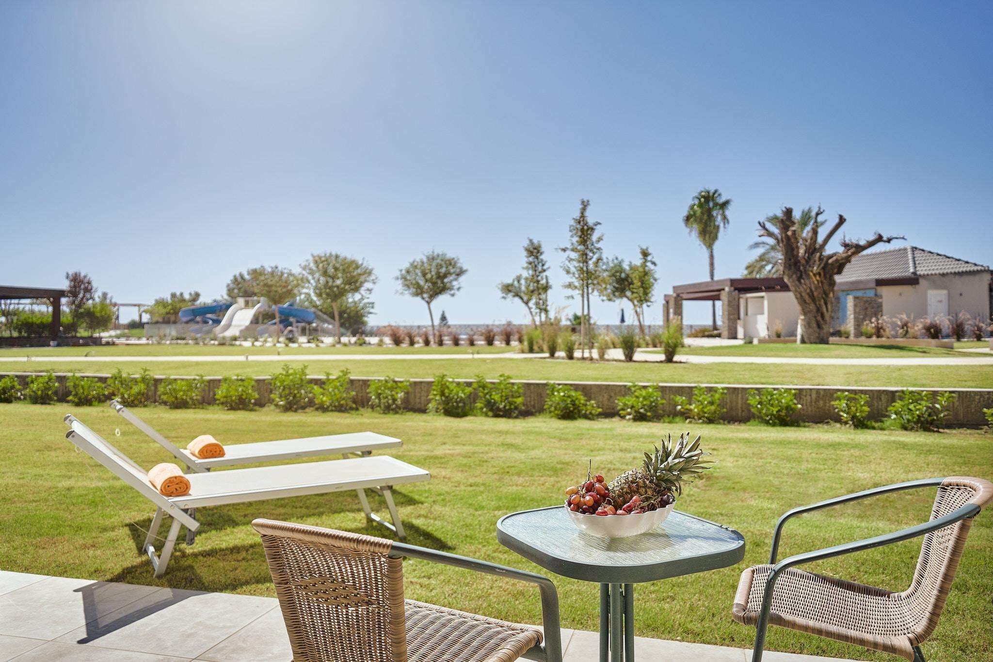 Un patio con dos sillones de descanso, una mesita con un frutero y vistas a un campo de golf y edificios al fondo.
