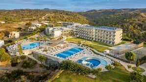 A resort with multiple swimming pools, a large building with balconies, and a hilly backdrop.