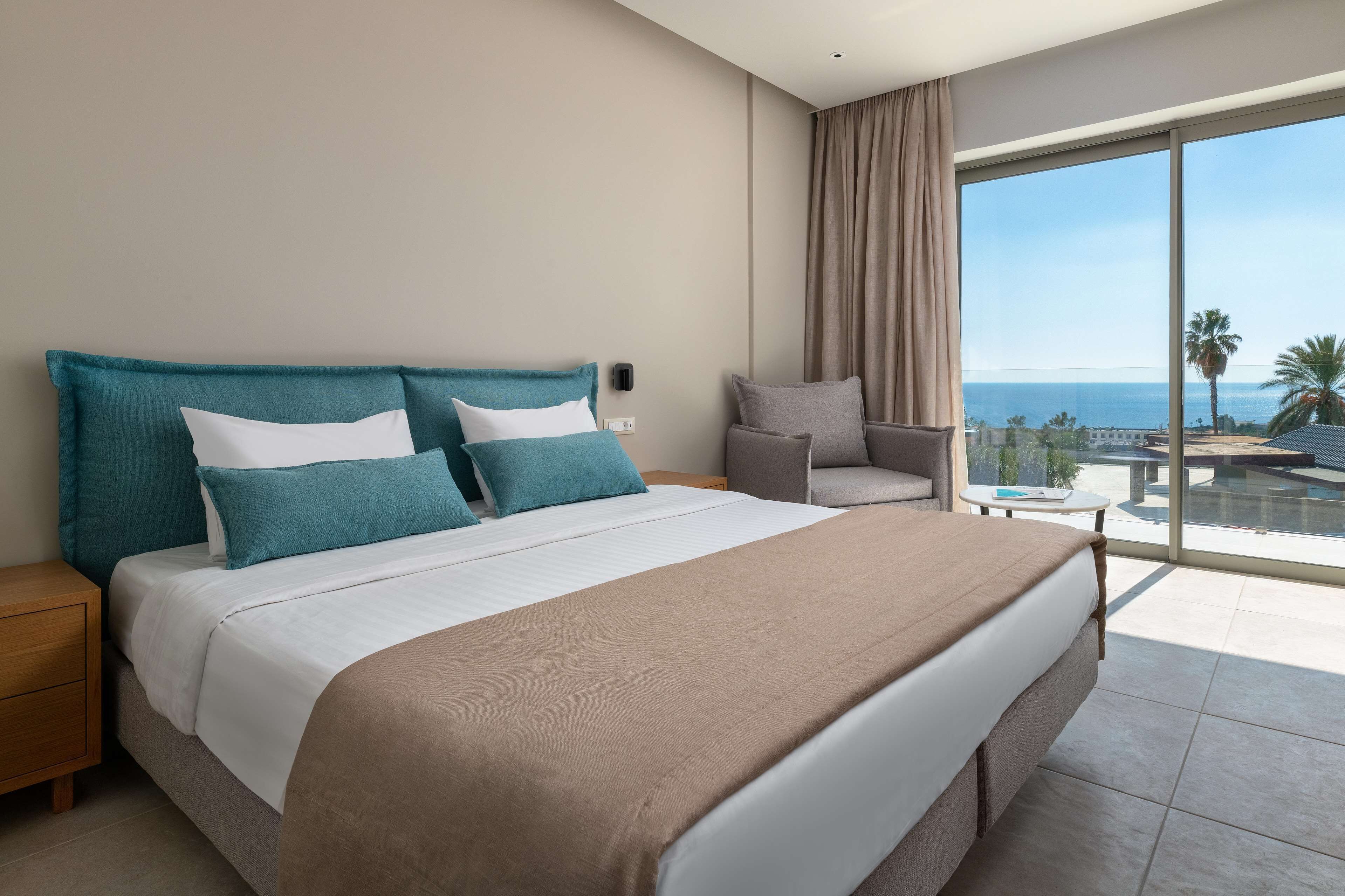 Habitación de hotel con una cama grande, una silla, una mesita y vista al océano.
