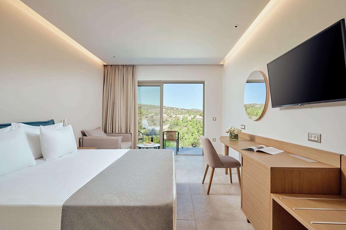 A hotel room with a bed, a desk, a television, and a view of the outdoors.