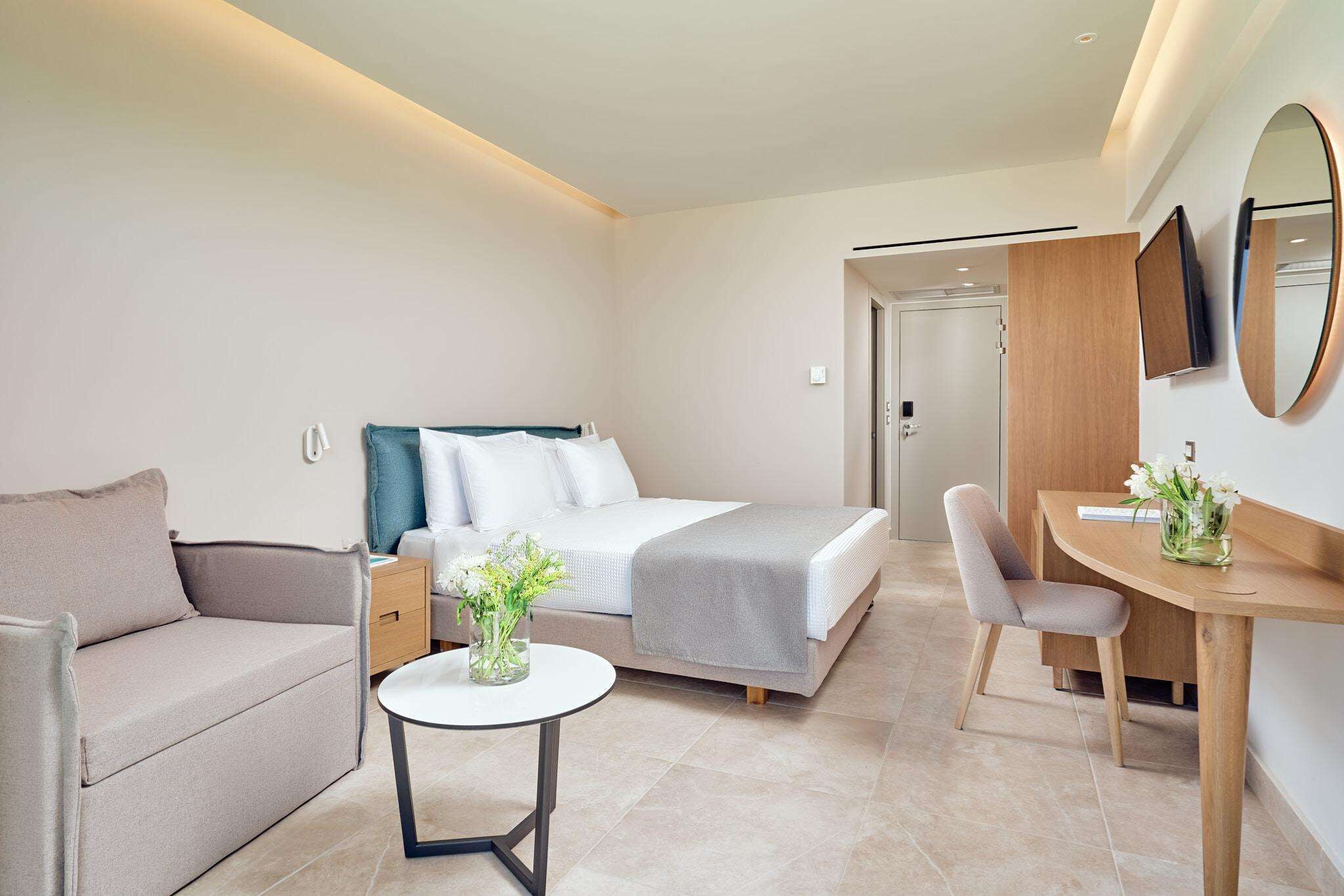 Moderni hotellihuone, jossa on sänky, sohva, työpöytä ja pieni pöytä.