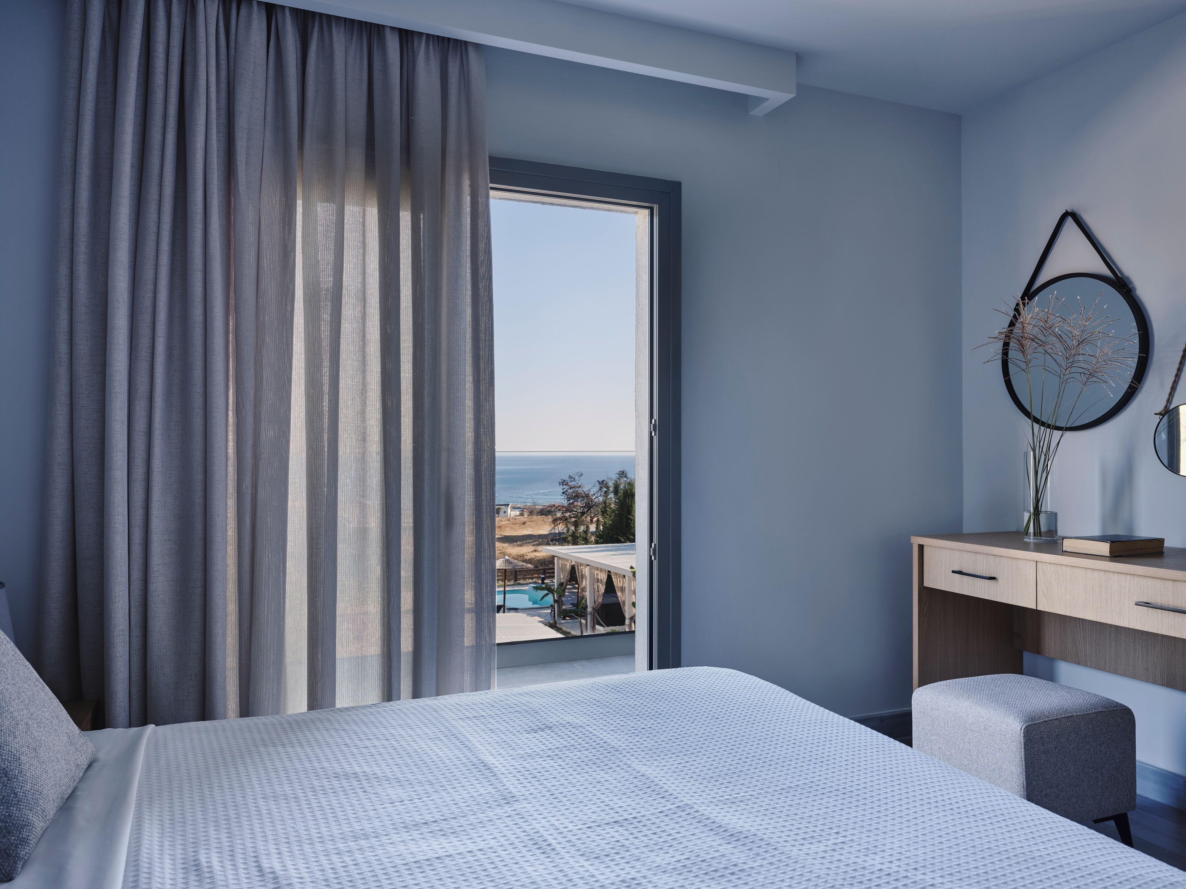 Een slaapkamer met een groot raam, een bed, een bureau en een stoel.