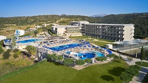A resort with multiple swimming pools, a large building with balconies, and a hilly landscape in the background.