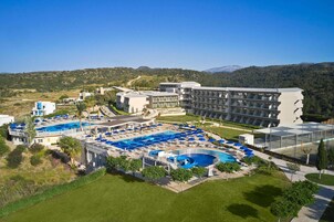 Un resort con varias piscinas, un edificio grande con balcones y un paisaje montañoso al fondo.