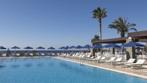 A pool area with lounge chairs and umbrellas, a clear sky, and palm trees.