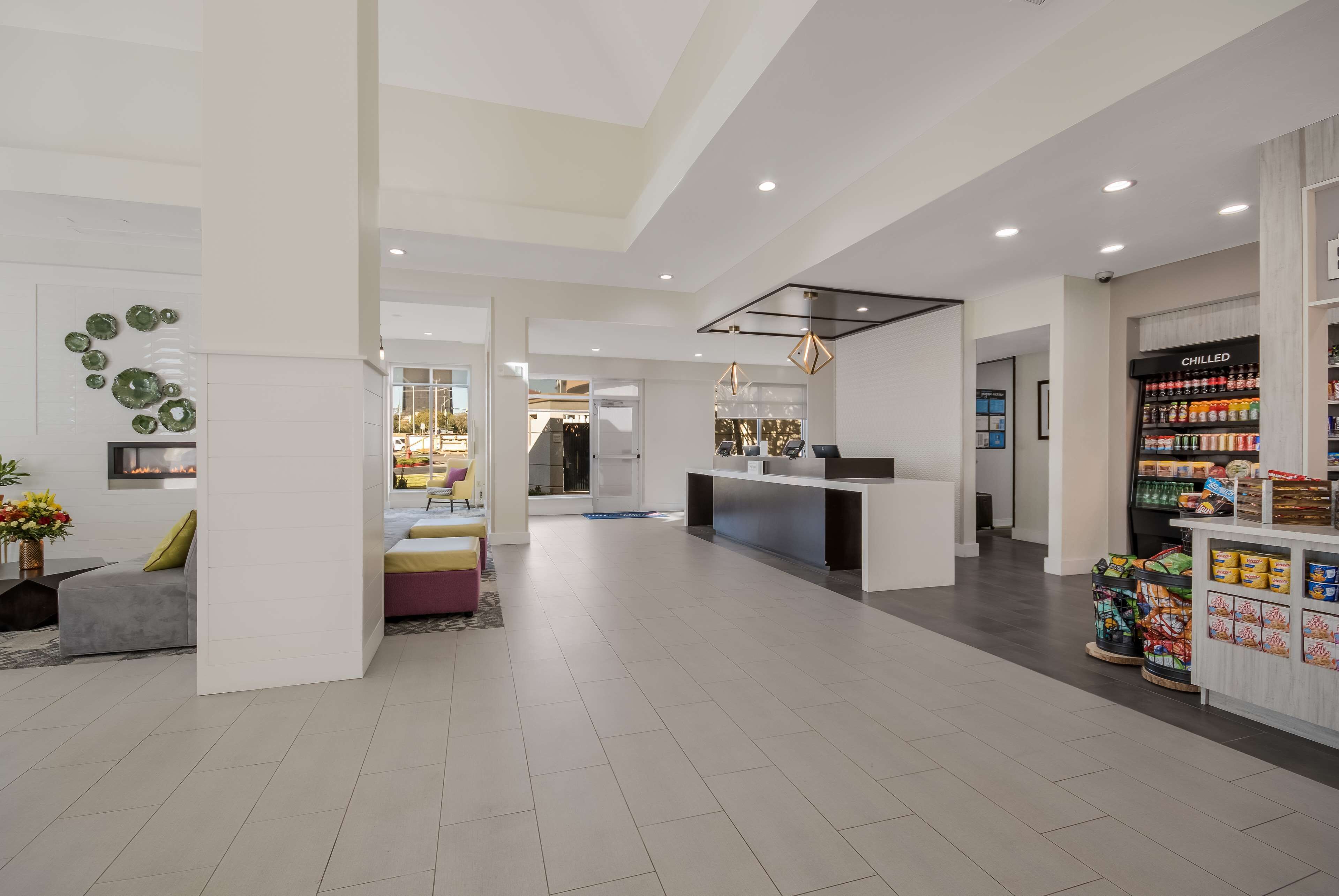 A spacious hotel lobby with a central seating area, a reception desk, and a food service counter.