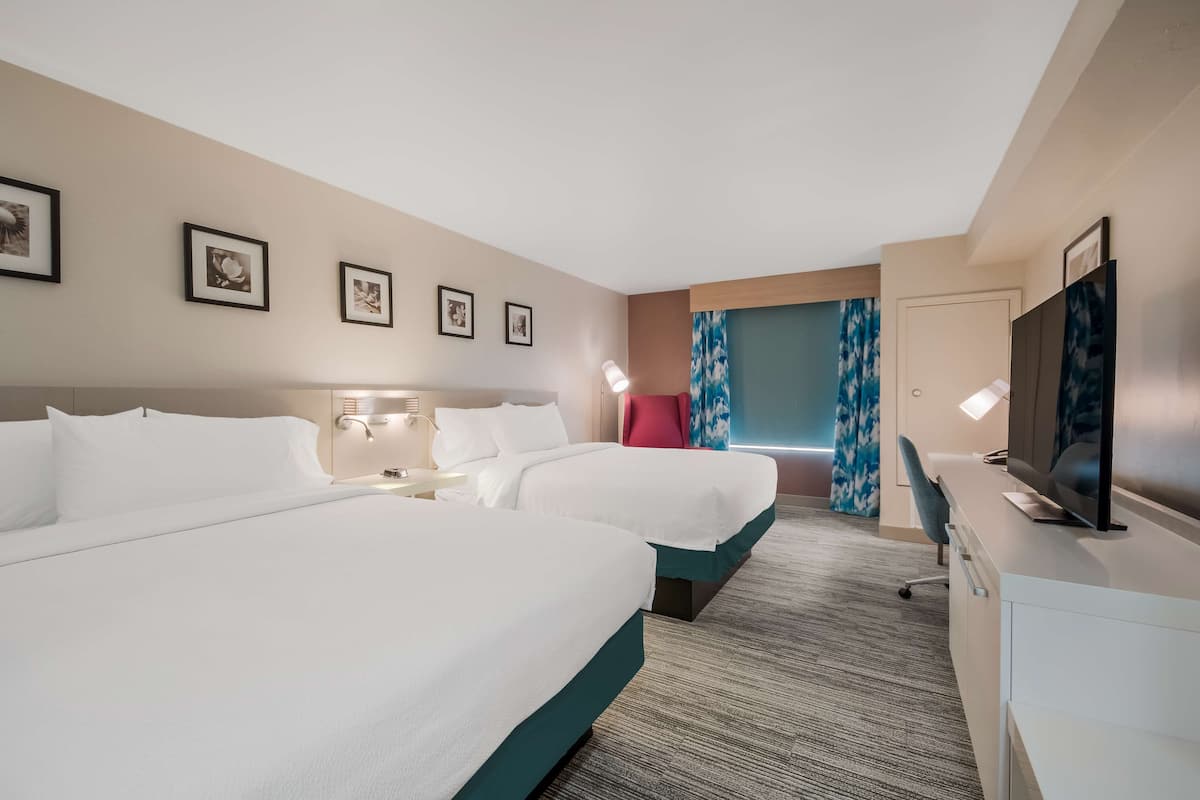A hotel room with two beds, a desk with a TV, and framed pictures on the wall.