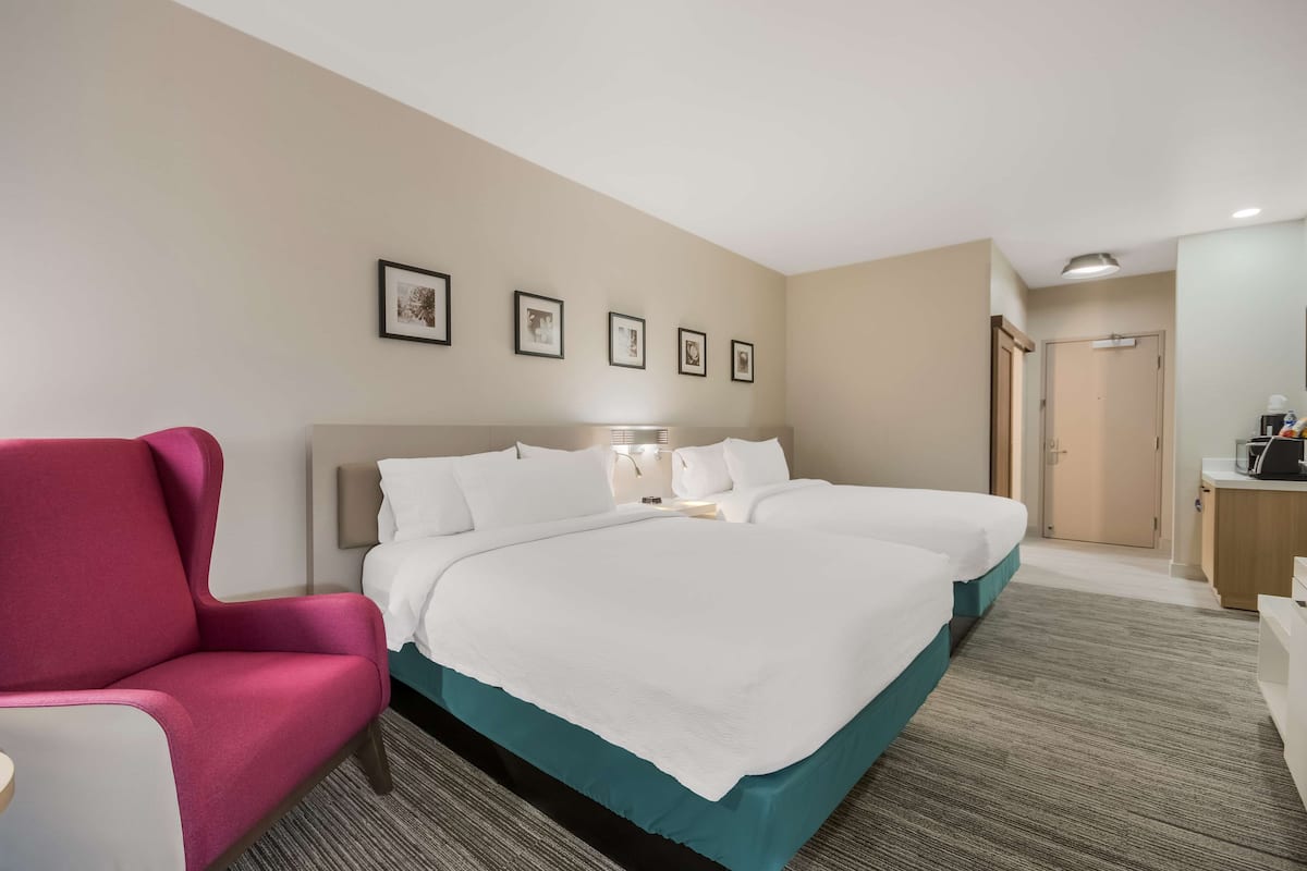 A hotel room with a large bed, a pink chair, a desk, and a door.