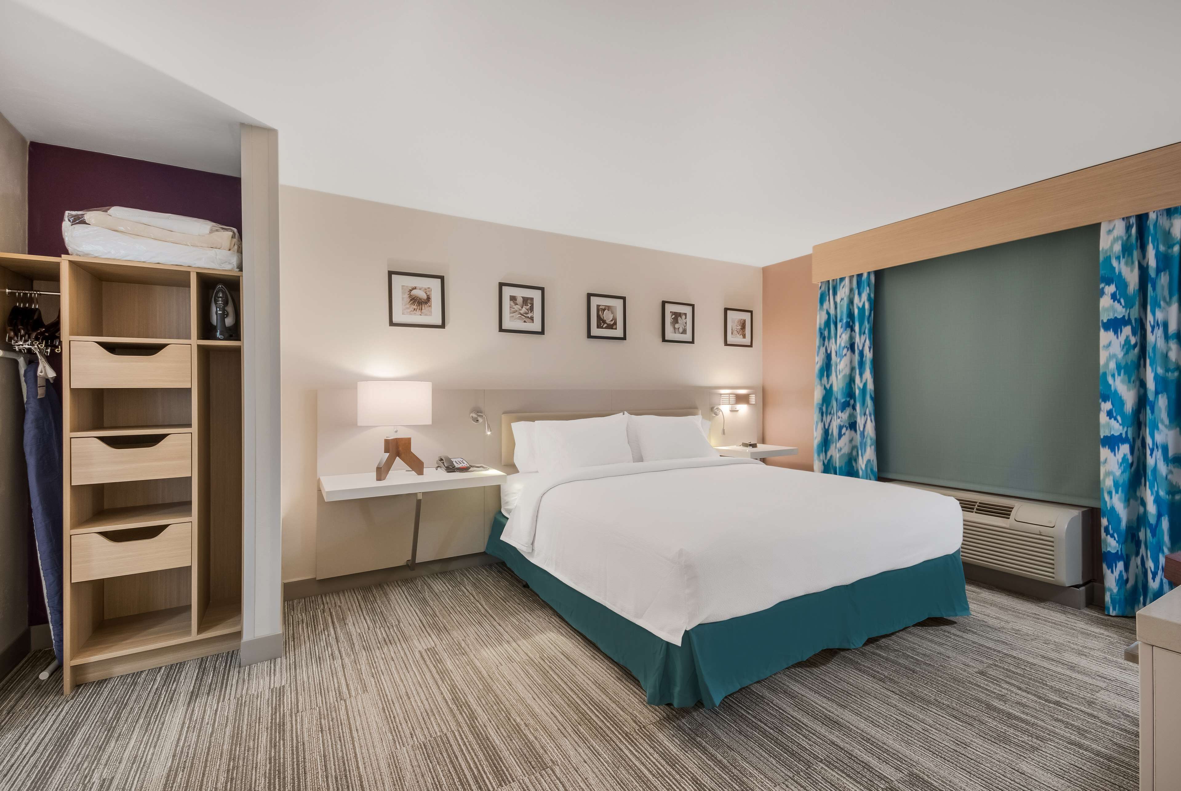 A hotel room with a bed, a wardrobe, a desk with a lamp, a TV, and a window with curtains.