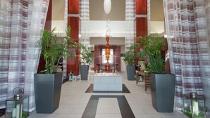 A spacious lobby with a central island, large potted plants, and a modern chandelier.