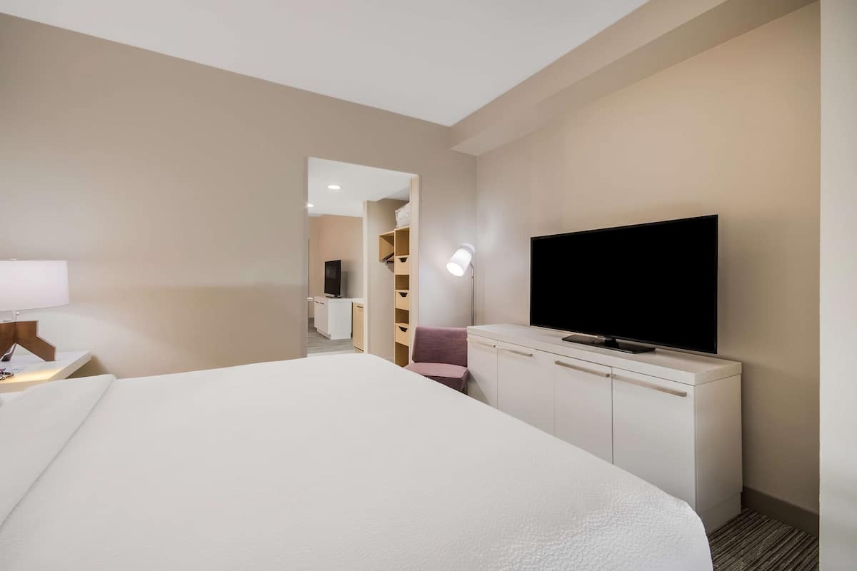 A hotel room with a large bed, a flat-screen TV, a bedside lamp, and a walk-in closet.