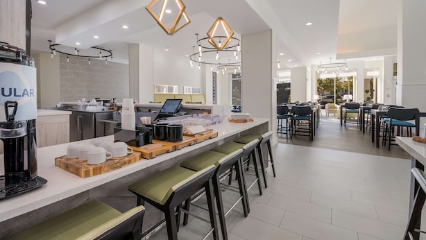 A modern hotel lobby with a central bar area, seating arrangements, and a reception desk.