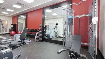 A gym with cardio machines, free weights, and a mirror.