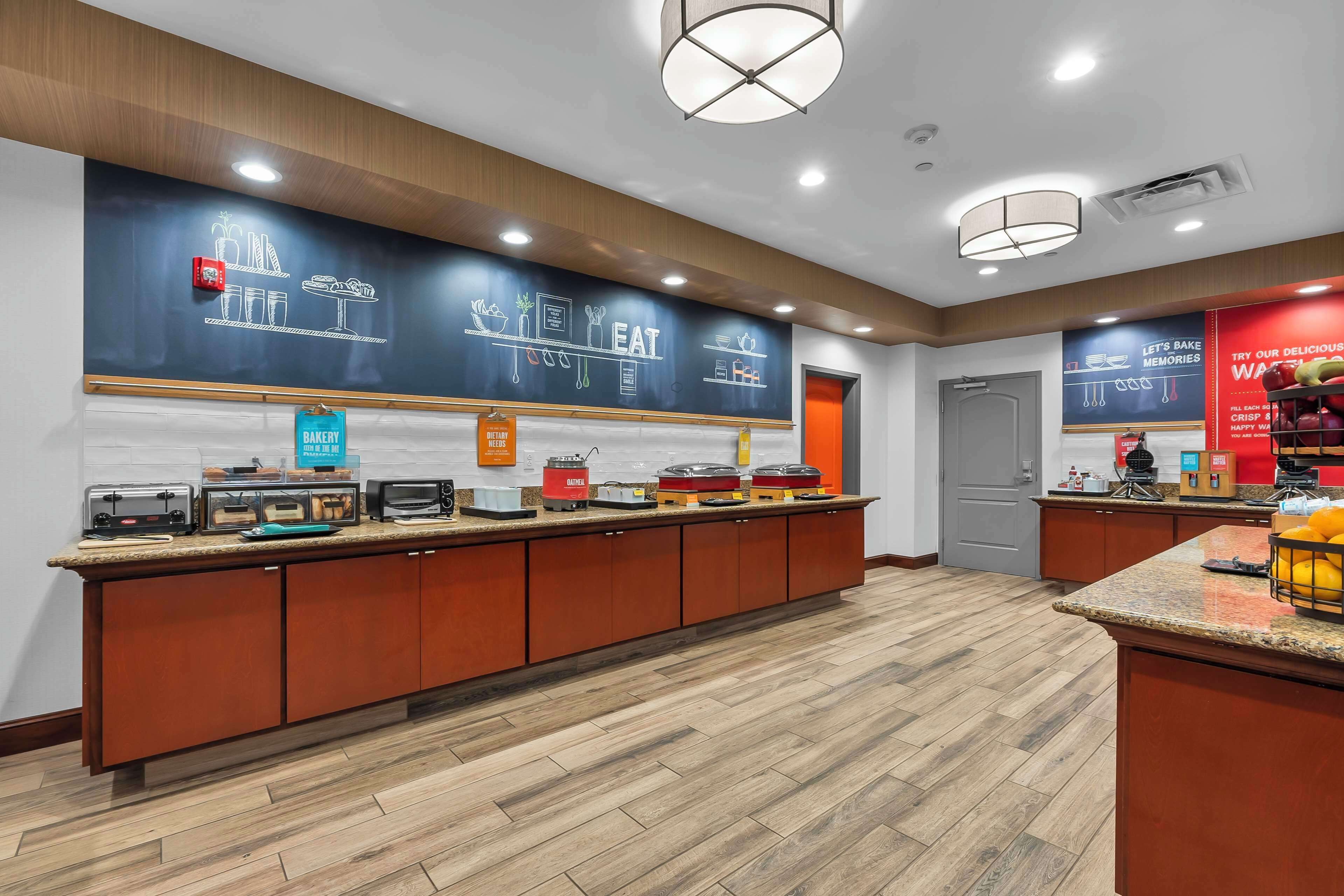 A breakfast bar with various food items and appliances, a sign indicating a bakery, and a wall with food-related illustrations.