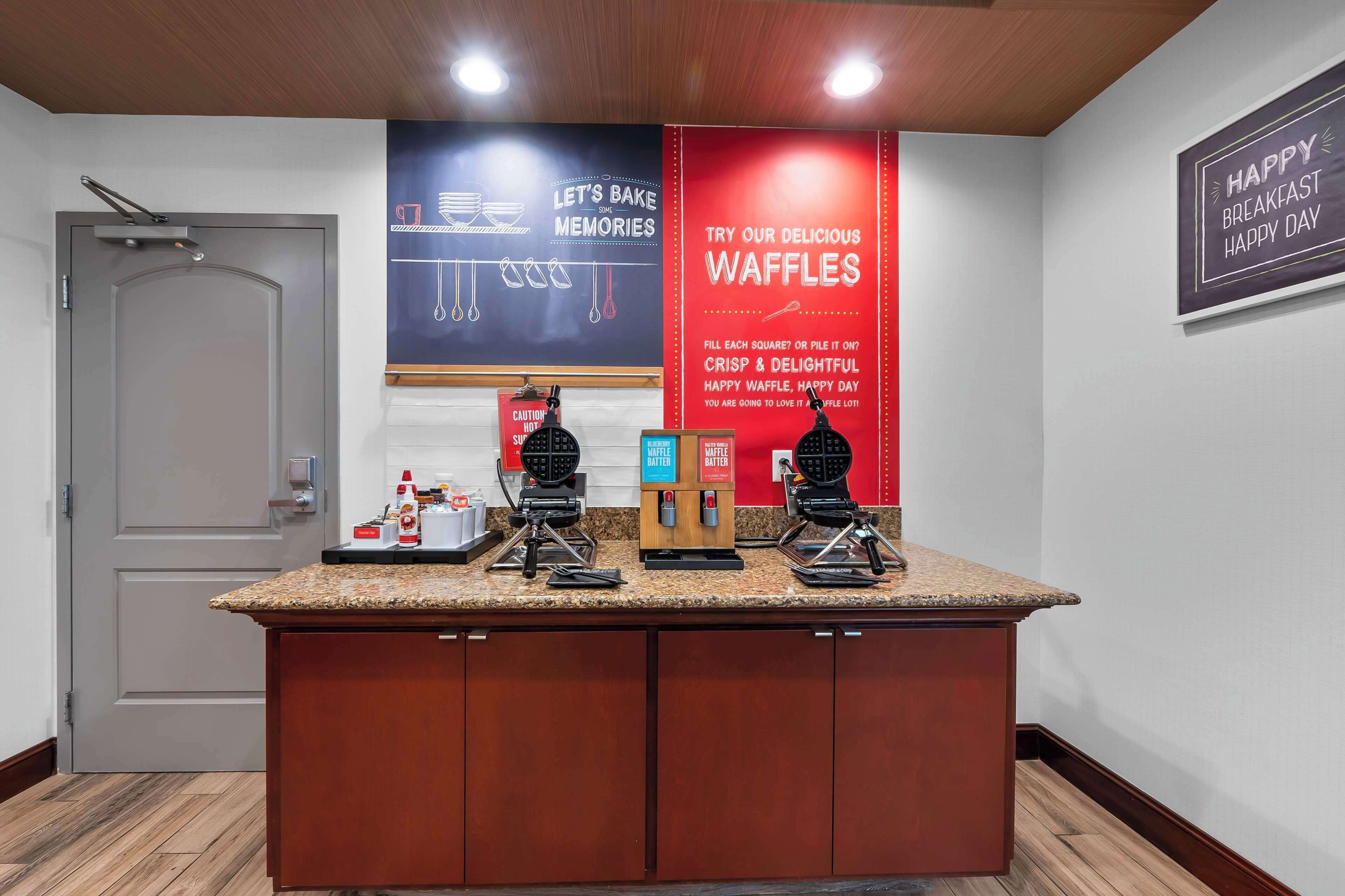 A kitchen area with waffle makers, a waffle station, and a sign promoting waffles.