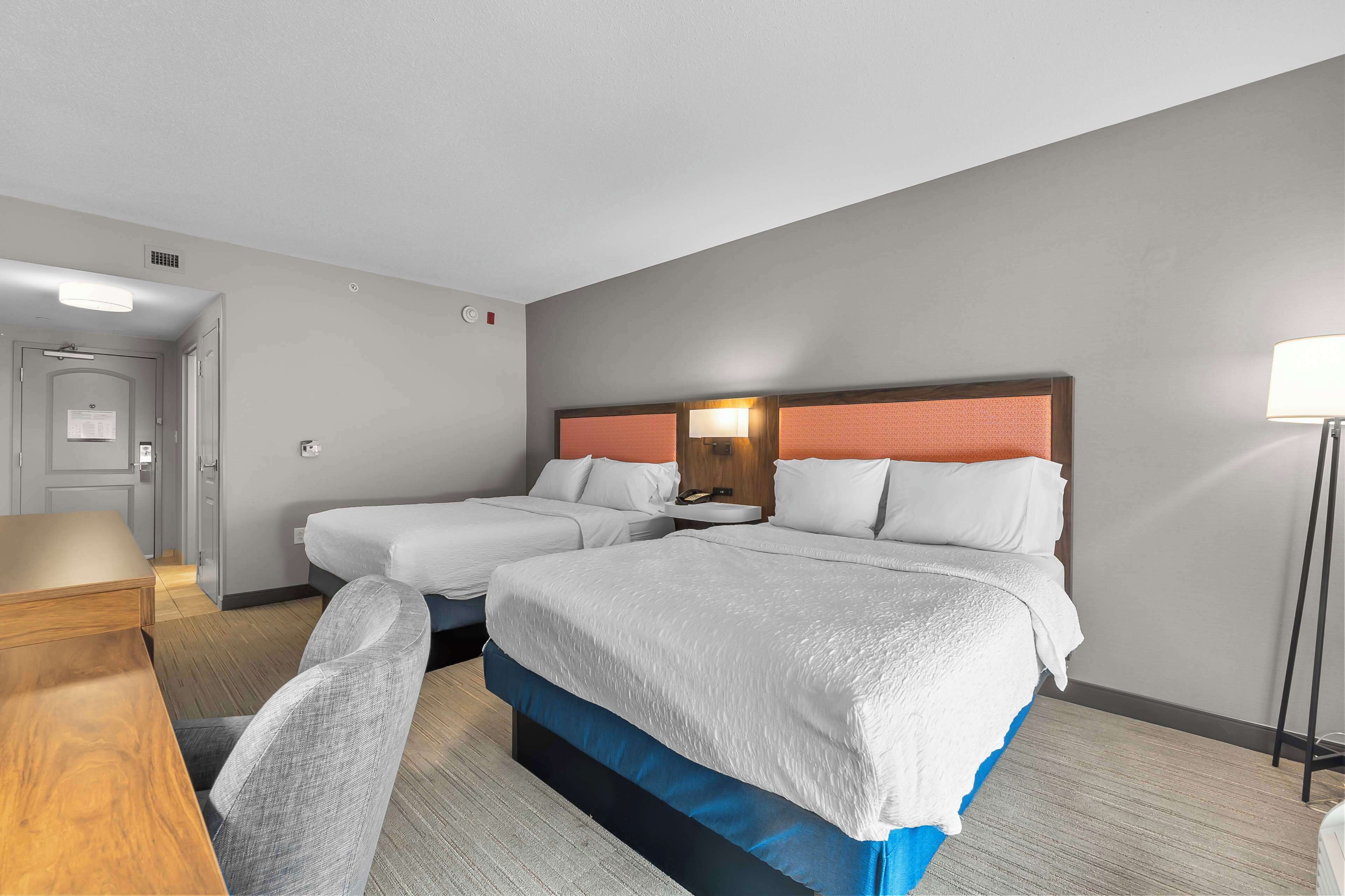A hotel room with two beds, a desk, and a chair.