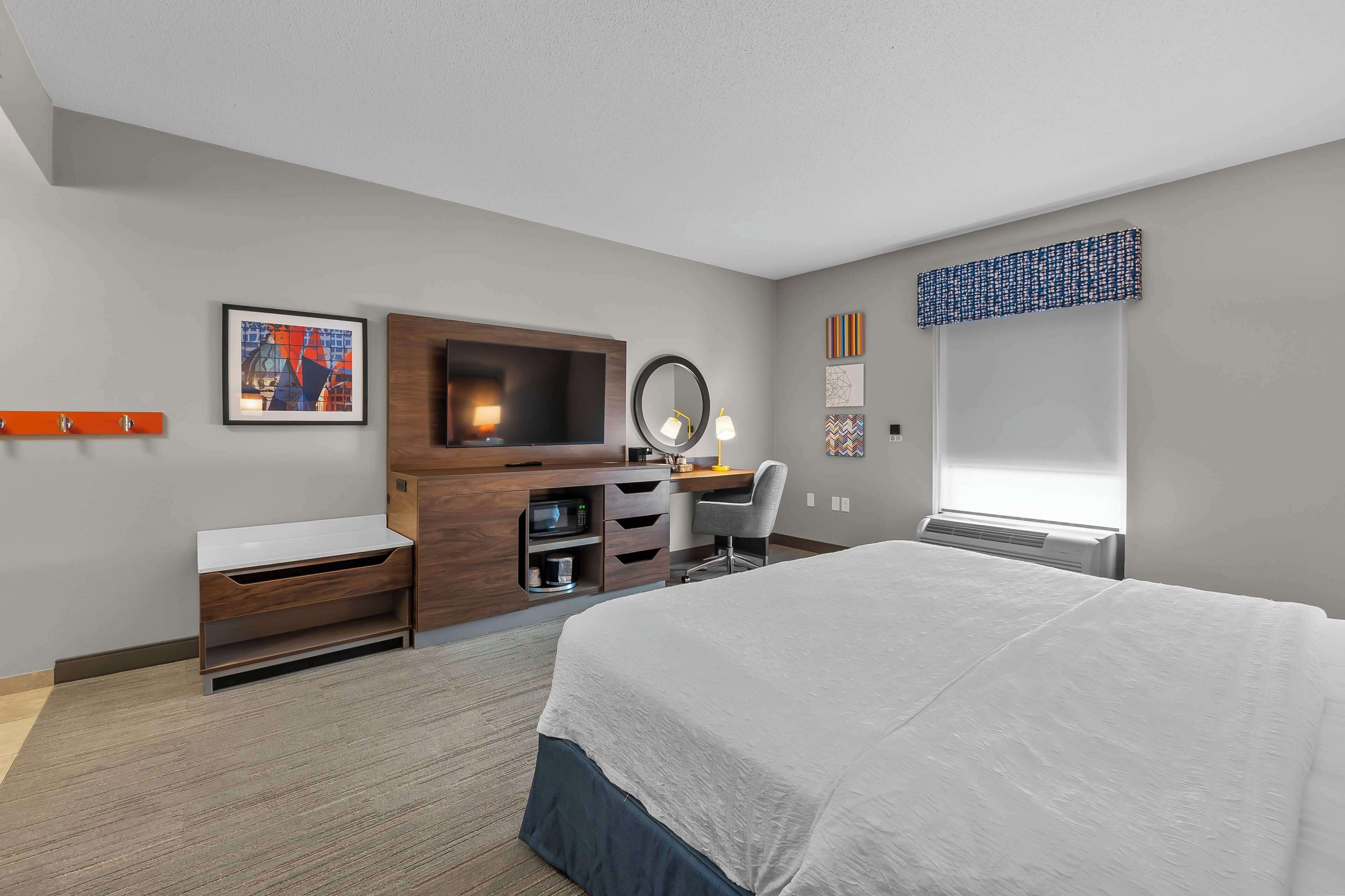Habitación de hotel con cama, escritorio, silla y un amplio ventanal.