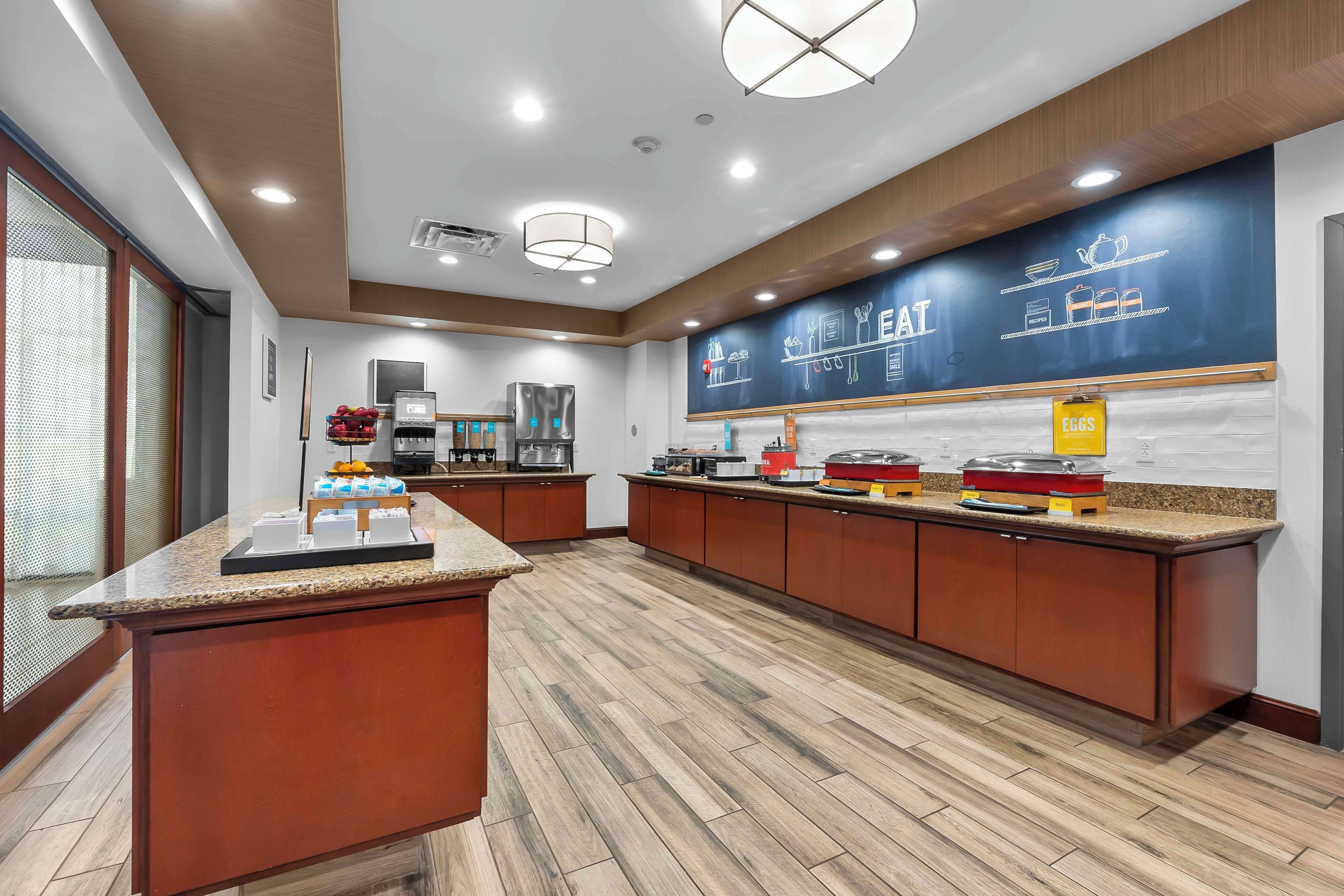 A modern kitchen with wooden cabinets, granite countertops, and a chalkboard wall displaying menu items.