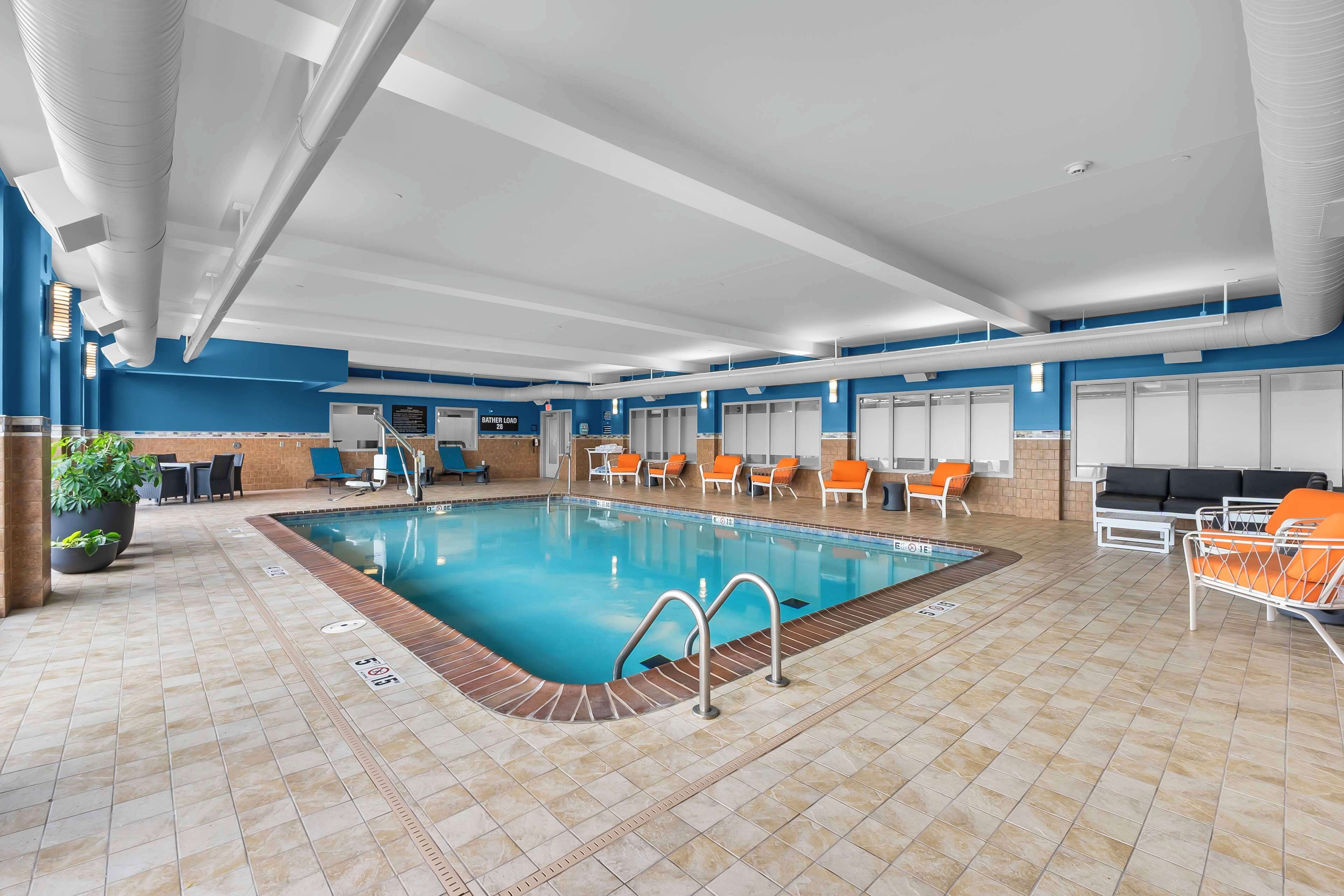 Una piscina interior con suelo de baldosas, sillones de descanso y una zona de estar con sofá.