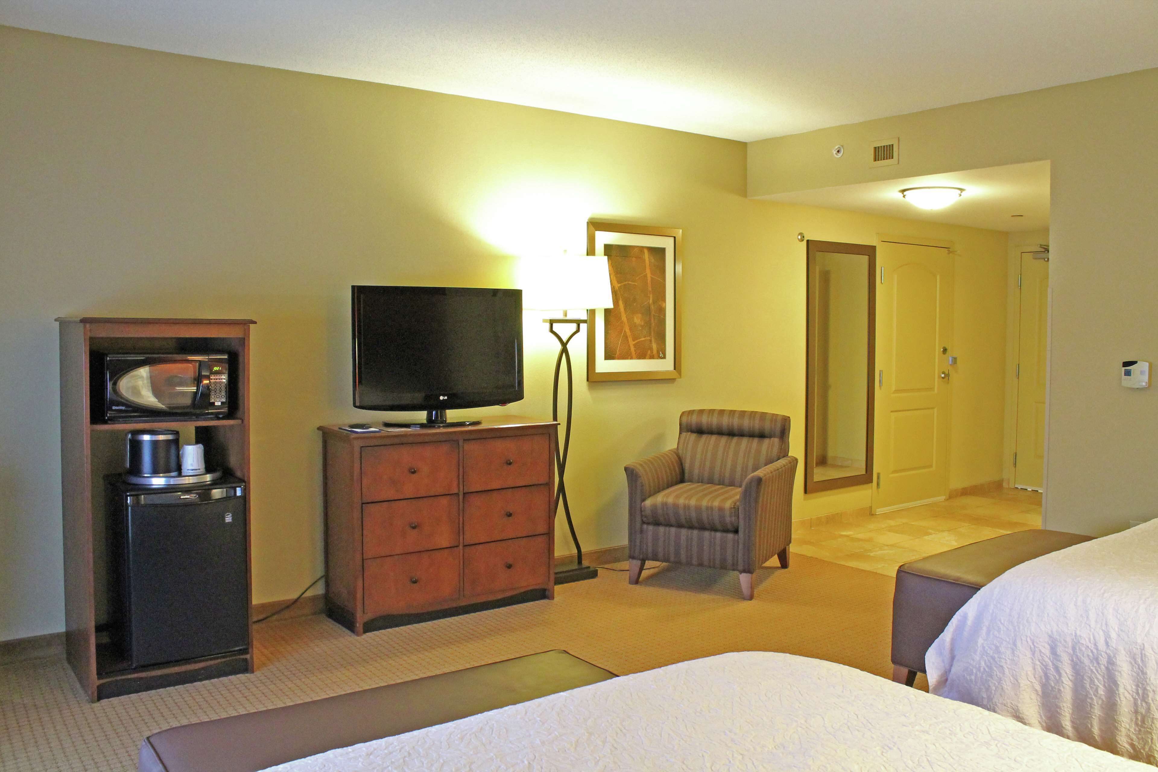 A hotel room with a bed, a television on a dresser, a chair, and a door leading to another room.