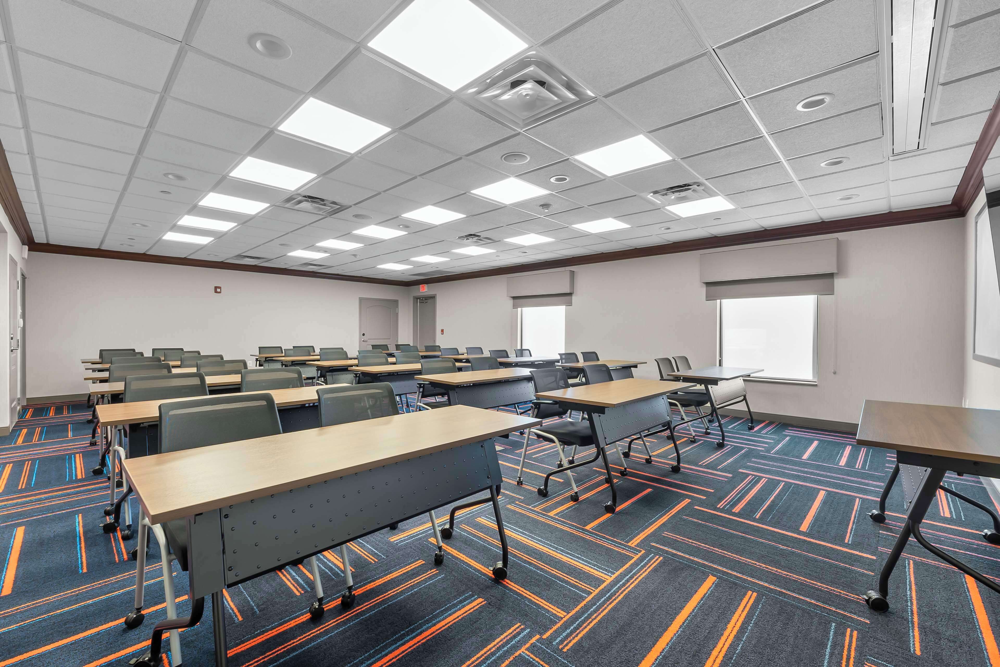 A conference room with multiple tables and chairs, a patterned carpet, and a ceiling with recessed lighting.
