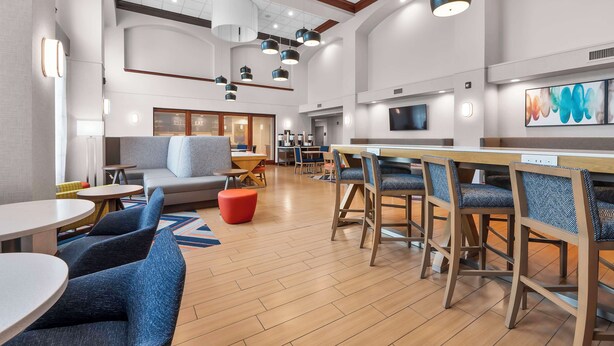 A spacious lobby with a high ceiling, modern lighting fixtures, a seating area with sofas and chairs, and a bar area with stools. - Hampton Inn & Suites St. Louis/South I-55 (St. Louis)