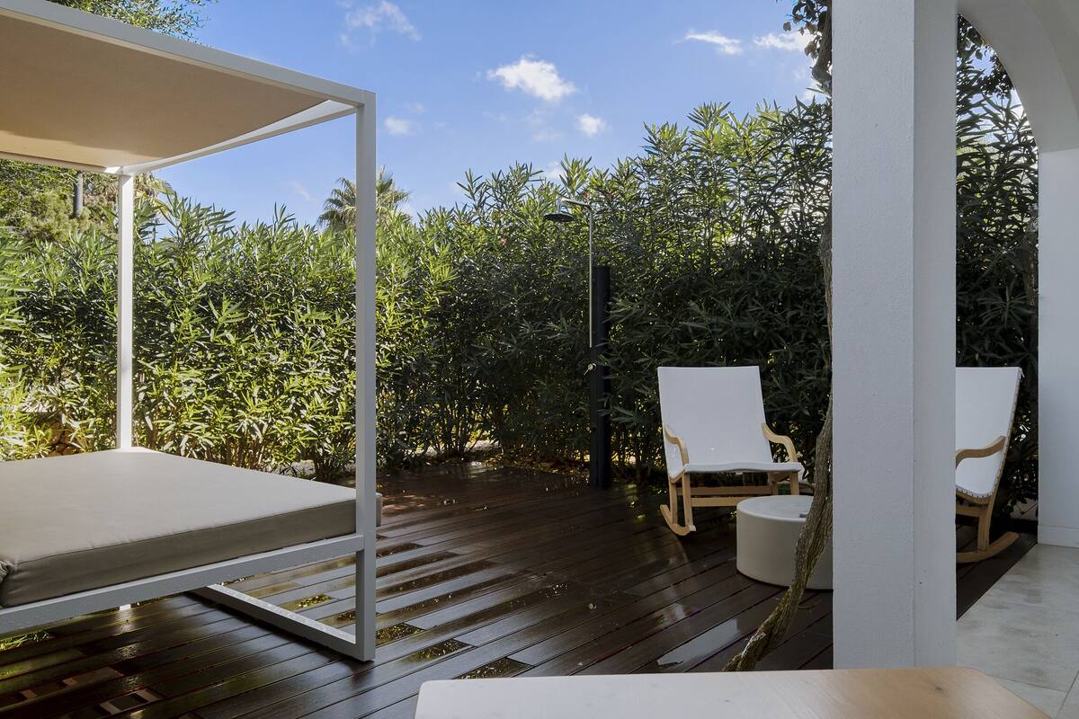 Une terrasse dotée d’une plateforme en bois, de sièges blancs rembourrés et d’une végétation luxuriante en arrière-plan.