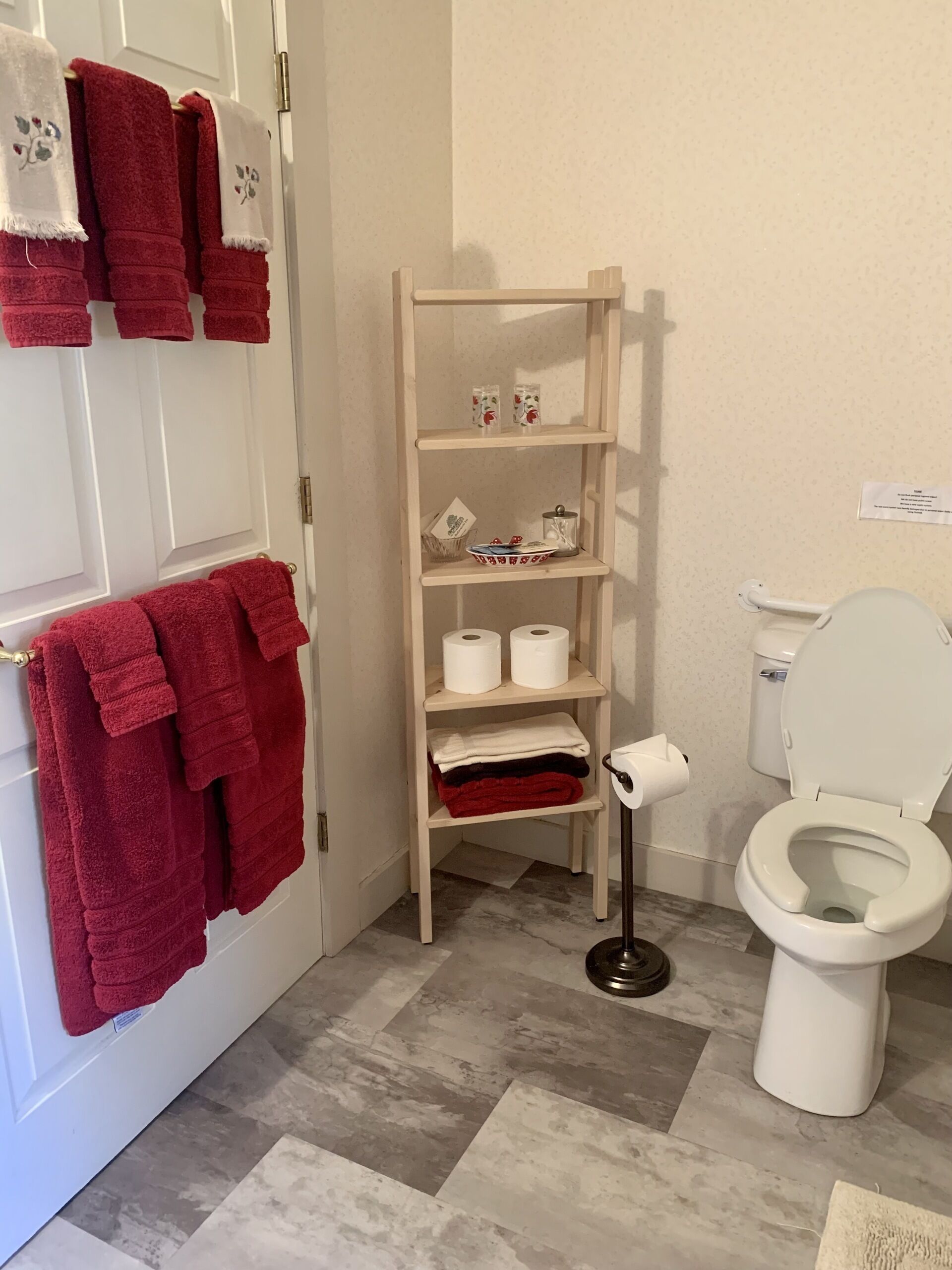 A bathroom with a toilet, a shelf with towels and toiletries, and a patterned floor.
