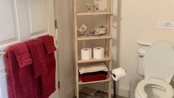 A bathroom with a toilet, a shelf with towels and toiletries, and a patterned floor.