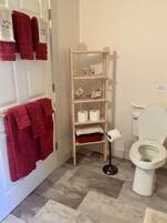 Un baño con inodoro, estante con toallas y artículos de aseo, y suelo estampado.