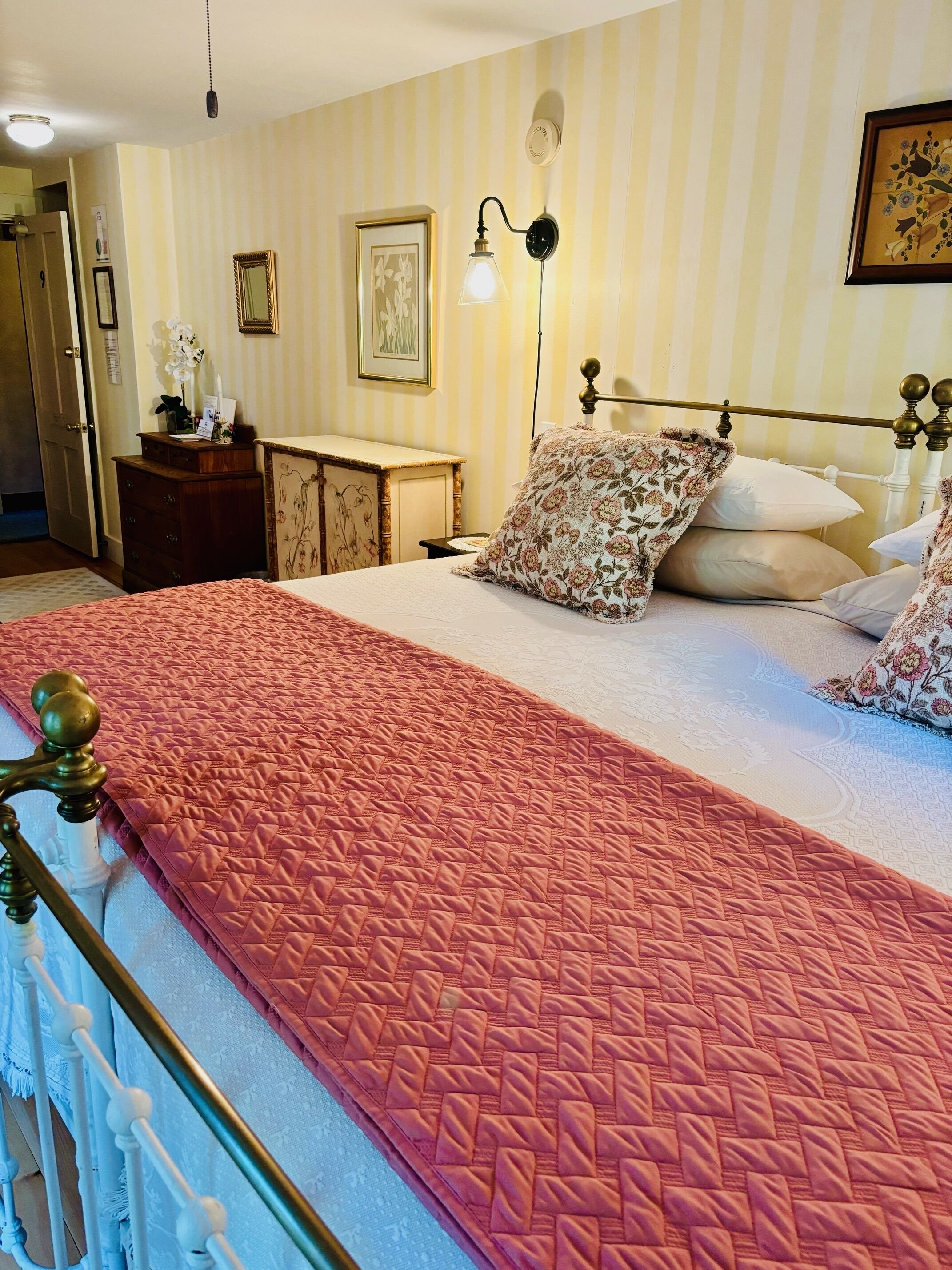 Une chambre à coucher avec un grand lit, une table de chevet, une commode et une lampe fixée au mur.