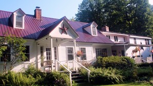 Ein zweistöckiges Haus mit einem roten Stern an der Fassade, einer Veranda mit Treppe und einem Garten davor.