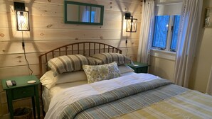 Ein gemütliches Schlafzimmer mit einem Holz-Kopfteil, einem grünen Nachttisch, einem Beistelltisch, einer gestreiften Bettdecke und einem Fenster mit Vorhängen.