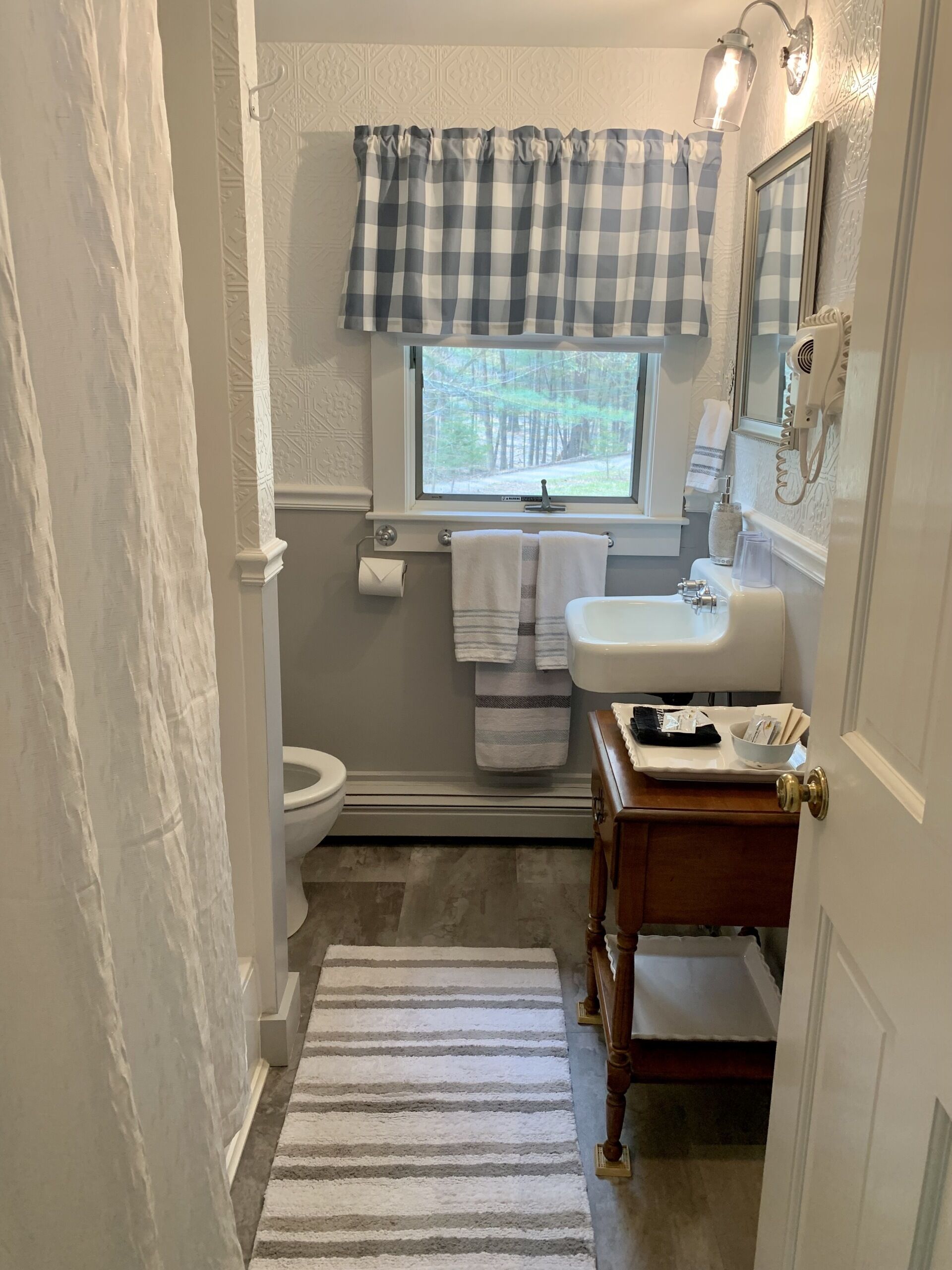 A bathroom with a toilet, sink, vanity, and a window with a view of trees.