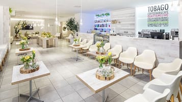 A modern coffee bar with white chairs and tables, a reception area, and a visible menu board.