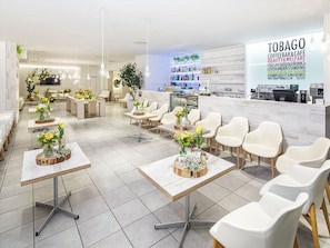 Un café moderne avec des chaises et des tables blanches, un espace d’accueil et un tableau des prix bien visible.