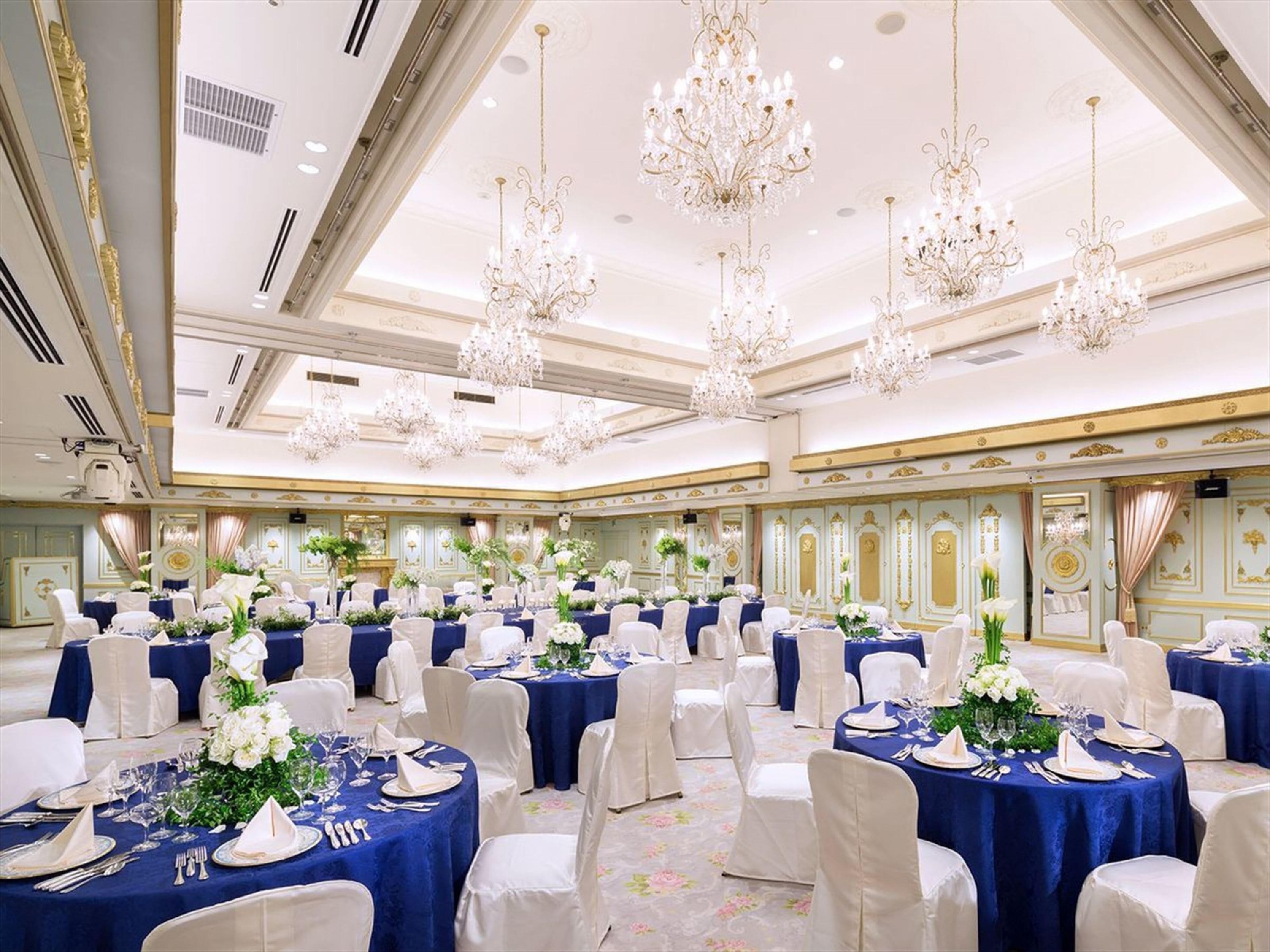 Une salle de banquet avec des tables rondes, des chaises blanches et des nappes bleues.