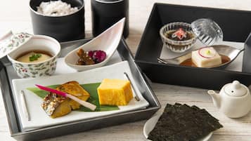 A tray with various Japanese dishes including fish, tofu, and seaweed, accompanied by small bowls of condiments and a teapot.