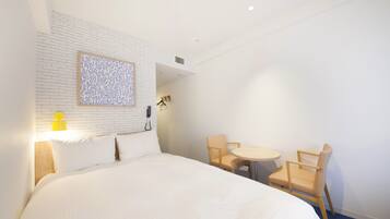 A hotel room with a large bed, two chairs, a small round table, a wall-mounted telephone, and a patterned artwork above the bed.