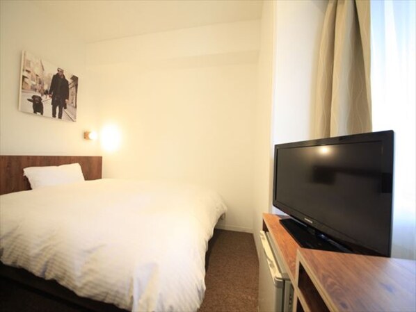 A hotel room with a bed, a flat-screen TV on a wooden stand, and a wall-mounted light. - Hotel Plumm (Yokohama)