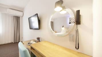 Habitación de hotel con un escritorio de madera, un espejo redondo con luz, un televisor de pantalla plana y un teléfono.