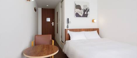 Habitación de hotel con una cama, un escritorio y una silla. Hay un cuadro en la pared y un teléfono sobre el escritorio.