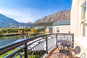 A balcony with a view of a lake, mountains, and a row of houses. - L'ermitage - Franschhoek Chateau & Villas (Franschhoek)