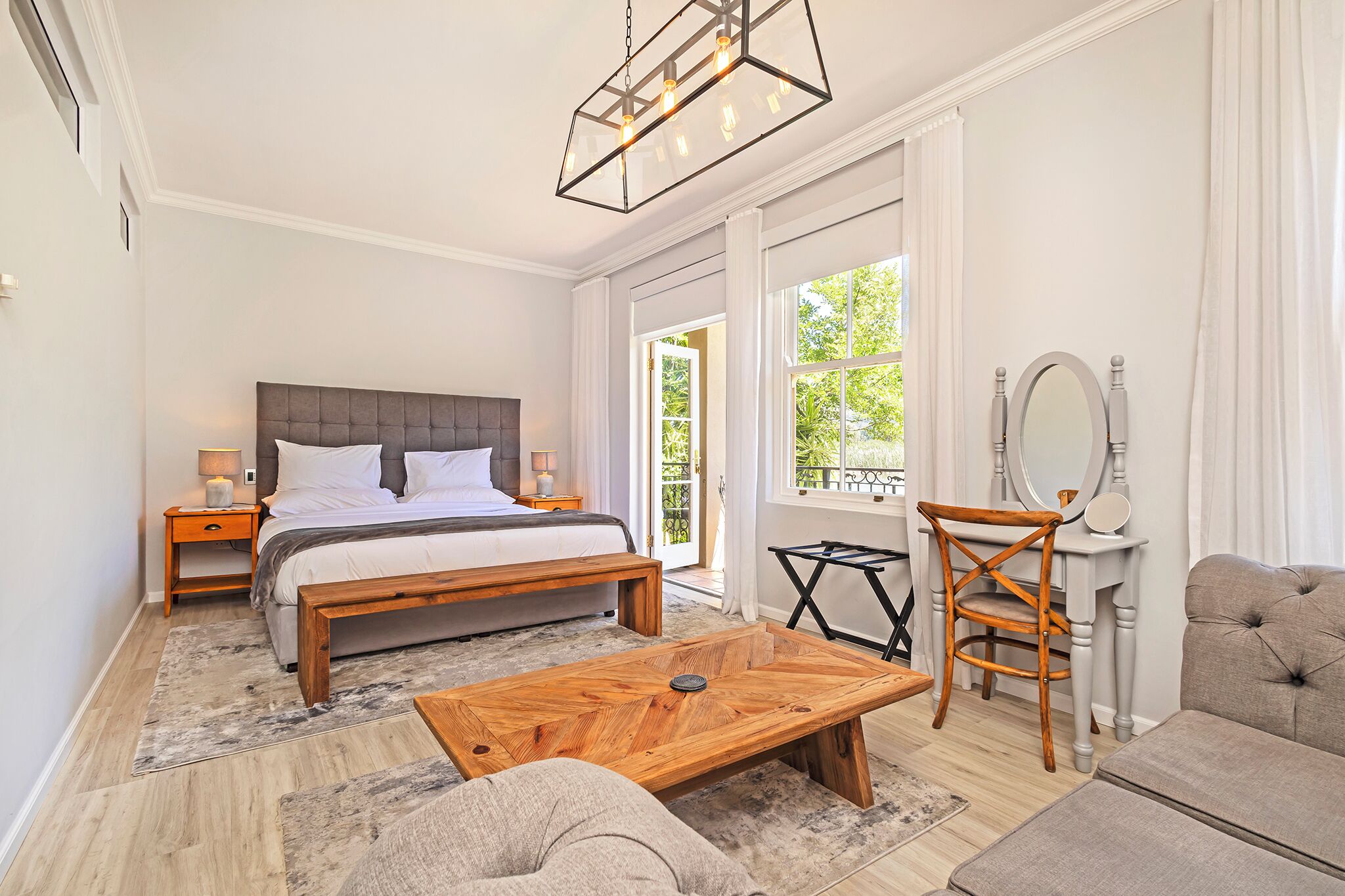 A bedroom with a large bed, bedside tables, a wooden coffee table, a chair, a sofa, and a mirror.
