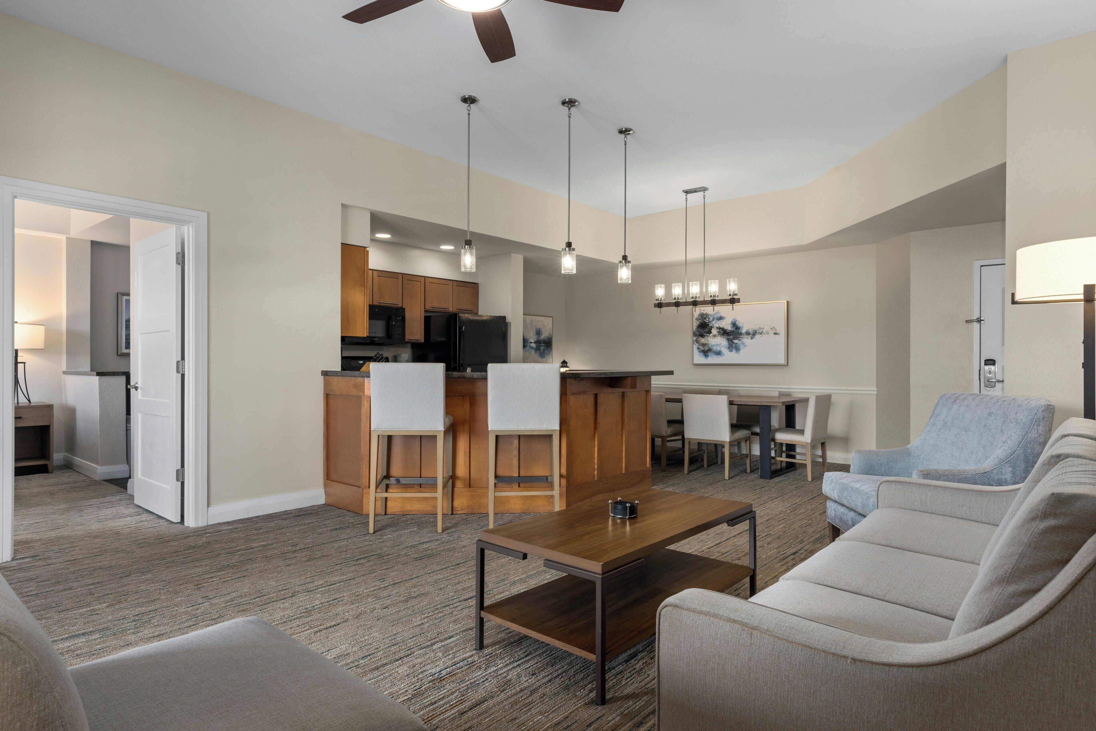 A modern living room with a sofa, a coffee table, and a dining area with a kitchen in the background.