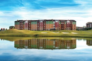 Een meerlaags hotel met een spiegelbeeld in stil water, omgeven door een golfbaan.