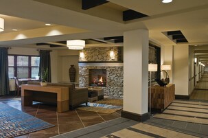 A hotel lobby with a stone fireplace, a dining area, and a hallway.