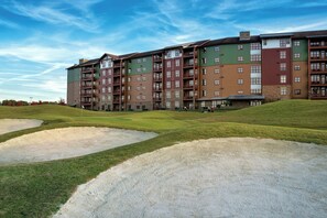 Een meerhoog hotel met een plat dak, grote ramen en een gazon met zandbunkers.